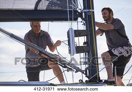 Stock Image - Men adjusting sailing equipment. Fotosearch