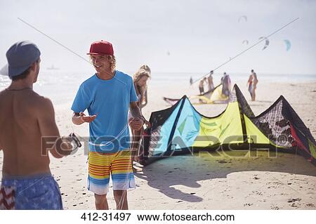 Stock Photo - Men preparing kiteboarding kite on sunny beach. Fotosearch