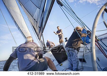 Stock Photo - Men sailing adjusting rigging and sail on sailboat. Fotosearch