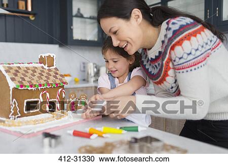 Stock Image - Mother and daughter decorating gingerbread house. Fotosearch