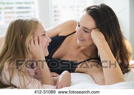 Stock Photo - Mother and daughter laying on bed talking. Fotosearch