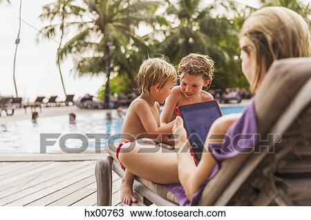 Stock Image - Mother and sons relaxing with digital tablet at poolside. Fotosearch
