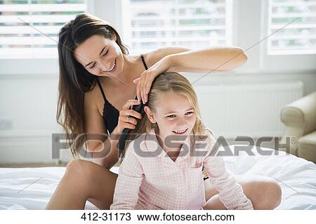 Stock Image - Mother brushing daughters hair on bed. Fotosearch