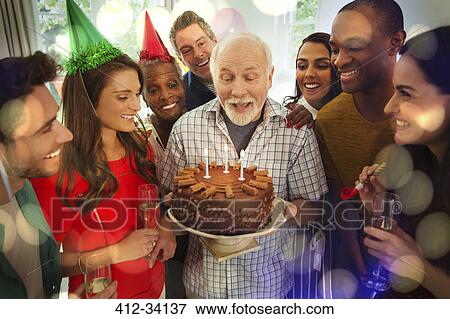 Multi-ethnic family watching senior man blow out birthday candles on chocolate cake View Large Photo Image Stock Photo - Multi-ethnic family watching senior man blow out birthday candles on chocolate cake. Fotosearch