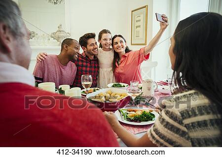 Stock Image - Multi-ethnic family with camera phone taking selfie at Christmas dinner table. Fotosearch