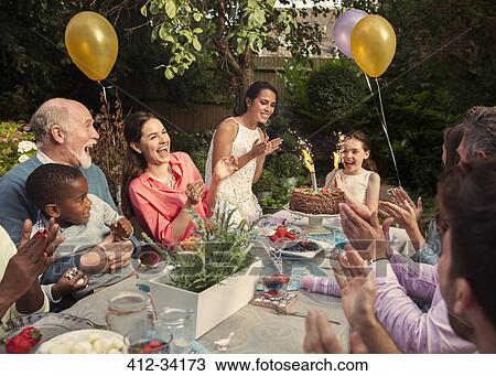 Multi-ethnic multi-generation family clapping celebrating birthday with fireworks cake at patio table View Large Photo Image Stock Image - Multi-ethnic multi-generation family clapping celebrating birthday with fireworks cake at patio table. Fotosearch