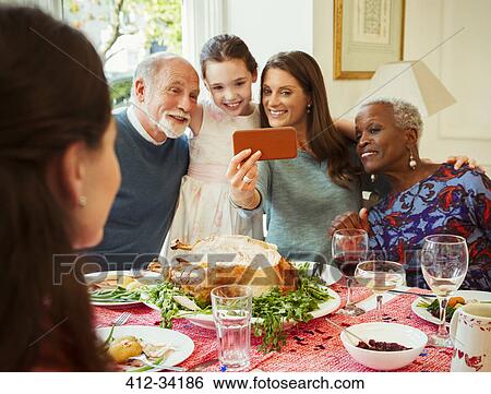 Stock Photograph - Multi-ethnic multi-generation family with camera phone taking selfie at Christmas dinner table. Fotosearch