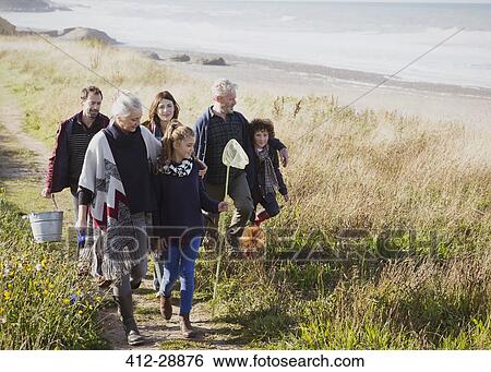 Stock Photograph - Multi-generation family walking with nets and bucket on sunny grass beach path. Fotosearch