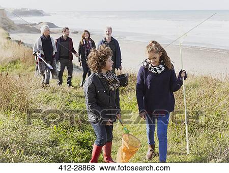 Stock Photo - Multi-generation family with nets walking on sunny grass beach path. Fotosearch