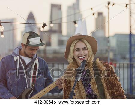 Stock Photography - Musicians playing guitar and singing at rooftop party. Fotosearch