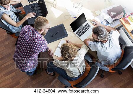 Overhead view design professionals working at laptops in meeting View Large Photo Image Picture - Overhead view design professionals working at laptops in meeting. Fotosearch