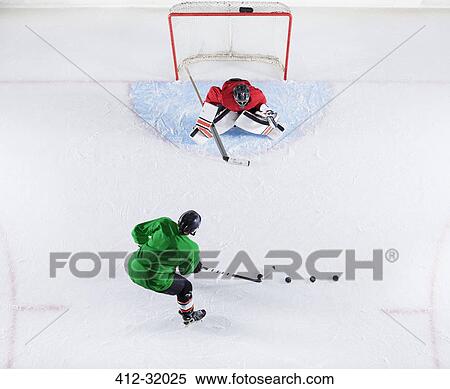 Stock Photography - Overhead view hockey player practicing with goalie shooting puck at goal net. Fotosearch