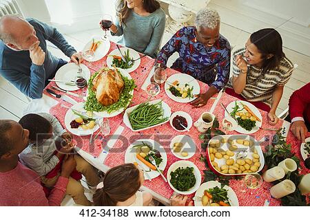 Stock Photo - Overhead view multi-ethnic multi-generation family enjoying Christmas dinner at table. Fotosearch