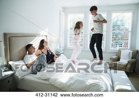 Parents watching children jumping on bed View Large Photo Image Stock Image - Parents watching children jumping on bed. Fotosearch
