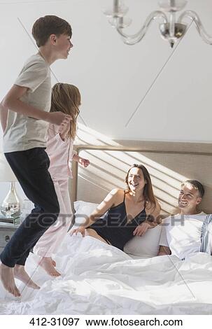 Stock Photo - Parents watching children jumping on bed. Fotosearch