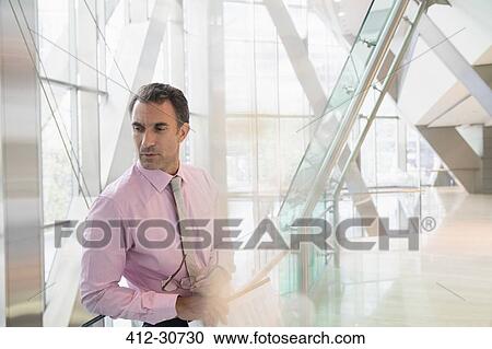 Stock Image - Pensive corporate businessman looking down in modern office lobby. Fotosearch