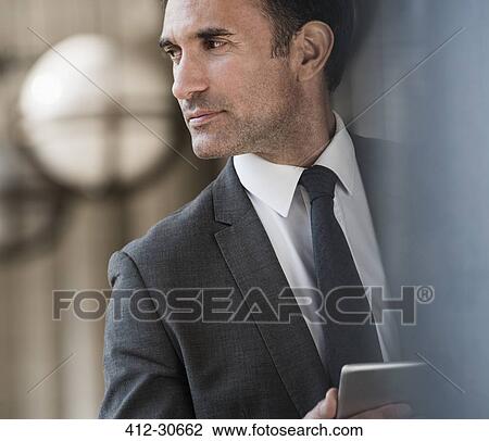 Stock Image - Pensive corporate businessman with digital tablet looking away. Fotosearch