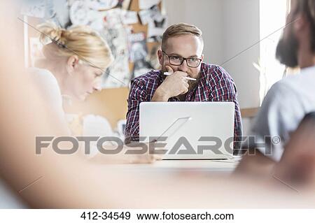 Stock Photo - Pensive design professional thinking at laptop. Fotosearch