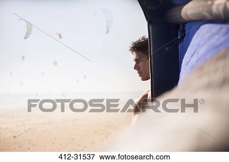 Stock Photo - Pensive man looking away behind kiteboarding kite on sunny beach. Fotosearch