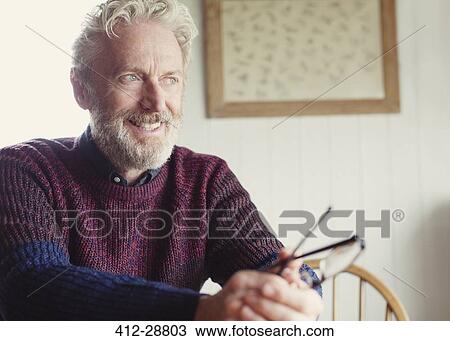 Stock Image - Pensive senior man holding eyeglasses and looking away. Fotosearch