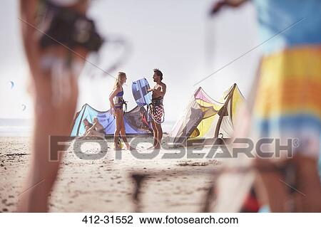 Stock Image - People with kiteboarding equipment talking on sunny beach. Fotosearch