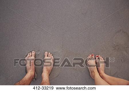 Stock Photo - Personal perspective barefoot couple standing in wet sand on beach. Fotosearch