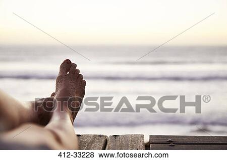 Stock Photo - Personal perspective barefoot woman with sand on foot and ocean view. Fotosearch