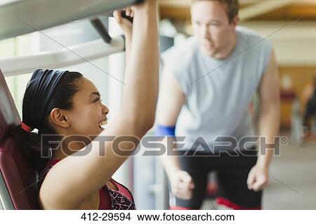 Picture - Personal trainer guiding enthusiastic woman using exercise equipment at gym. Fotosearch