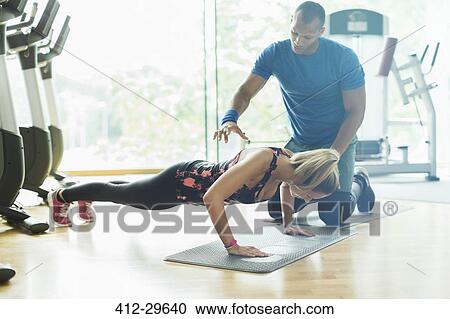 Personal trainer guiding woman doing push-ups at gym View Large Photo Image Stock Image - Personal trainer guiding woman doing push-ups at gym. Fotosearch