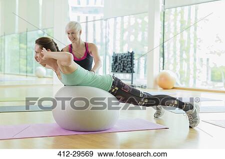 Personal trainer guiding woman doing back extensions on fitness ball View Large Photo Image Stock Photo - Personal trainer guiding woman doing back extensions on fitness ball. Fotosearch