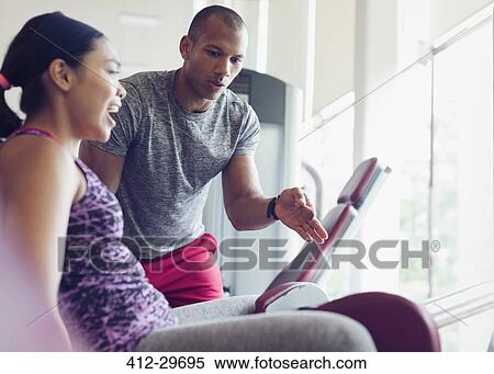 Stock Photography - Personal trainer guiding woman on exercise equipment at gym. Fotosearch