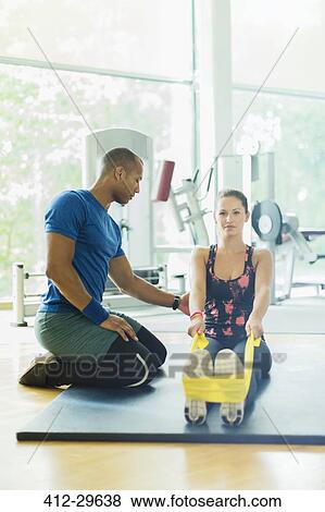 Personal trainer guiding woman stretching legs with resistance band at gym View Large Photo Image Stock Photo - Personal trainer guiding woman stretching legs with resistance band at gym. Fotosearch