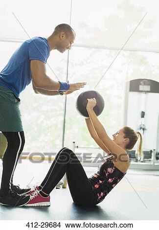 Personal trainer guiding woman with medicine ball at gym View Large Photo Image Picture - Personal trainer guiding woman with medicine ball at gym. Fotosearch