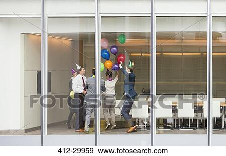 Playful business people in party hats celebrating with balloons in conference room View Large Photo Image Stock Photo - Playful business people in party hats celebrating with balloons in conference room. Fotosearch