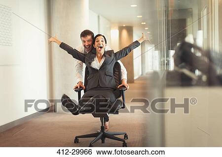 Playful businessman pushing exuberant businesswoman down corridor in office chair View Large Photo Image Stock Photograph - Playful businessman pushing exuberant businesswoman down corridor in office chair. Fotosearch