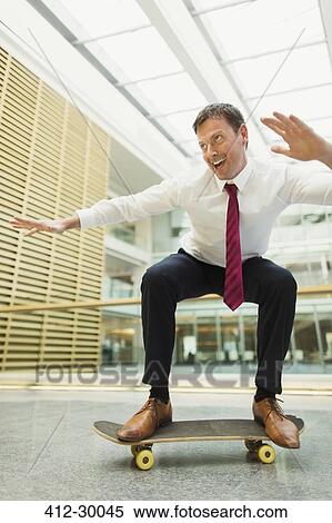 Playful businessman skateboarding in office View Large Photo Image Stock Photography - Playful businessman skateboarding in office. Fotosearch