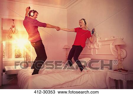 Playful couple dancing on bed listening to music with mp3 players and headphones View Large Photo Image Stock Image - Playful couple dancing on bed listening to music with mp3 players and headphones. Fotosearch