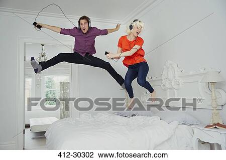 Playful couple jumping on bed and listening to music with mp3 player and headphones View Large Photo Image Stock Image - Playful couple jumping on bed and listening to music with mp3 player and headphones. Fotosearch