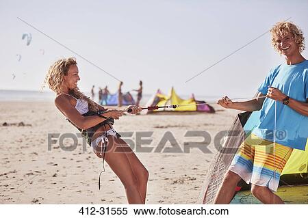 Playful couple preparing kiteboarding equipment on sunny beach View Large Photo Image Stock Photography - Playful couple preparing kiteboarding equipment on sunny beach. Fotosearch