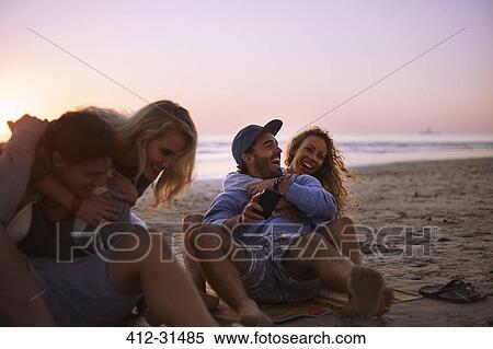 Stock Photography - Playful couples hanging out on sunset beach. Fotosearch