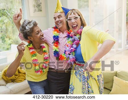 Stock Image - Playful mature adults dancing with leis in living room. Fotosearch