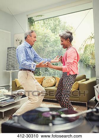 Playful mature couple dancing behind record player in living room View Large Photo Image Stock Image - Playful mature couple dancing behind record player in living room. Fotosearch