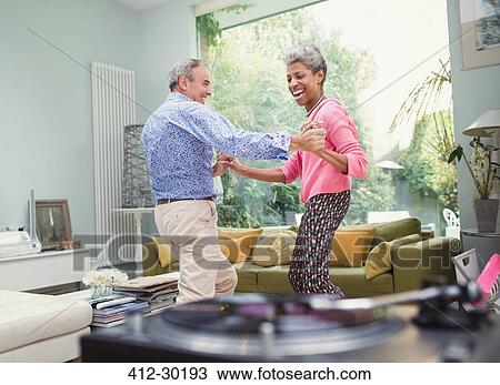 Playful mature couple dancing in living room View Large Photo Image Stock Image - Playful mature couple dancing in living room. Fotosearch