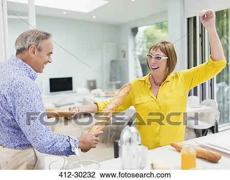 Playful mature couple sword fighting with baguettes in kitchen View Large Photo Image Stock Image - Playful mature couple sword fighting with baguettes in kitchen. Fotosearch
