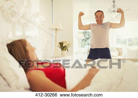Playful mature man flexing muscles for wife in bedroom View Large Photo Image Stock Photograph - Playful mature man flexing muscles for wife in bedroom. Fotosearch