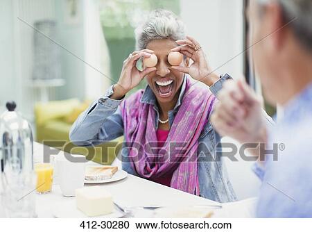 Playful mature woman covering eyes with eggs at breakfast table View Large Photo Image Stock Image - Playful mature woman covering eyes with eggs at breakfast table. Fotosearch