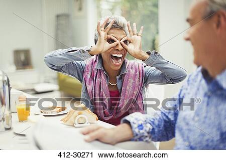 Playful mature woman gesturing finger glasses at breakfast table View Large Photo Image Stock Image - Playful mature woman gesturing finger glasses at breakfast table. Fotosearch