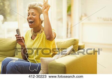 Playful mature woman listening to headphones with MP3 player in living room View Large Photo Image Stock Image - Playful mature woman listening to headphones with MP3 player in living room. Fotosearch