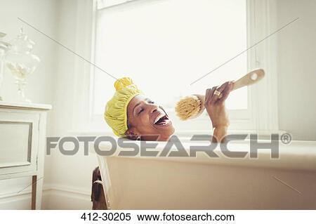 Playful mature woman singing into loofah brush in bathtub View Large Photo Image Stock Photography - Playful mature woman singing into loofah brush in bathtub. Fotosearch