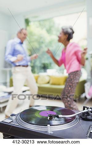Stock Image - Playful nature couple dancing in living room behind record player. Fotosearch